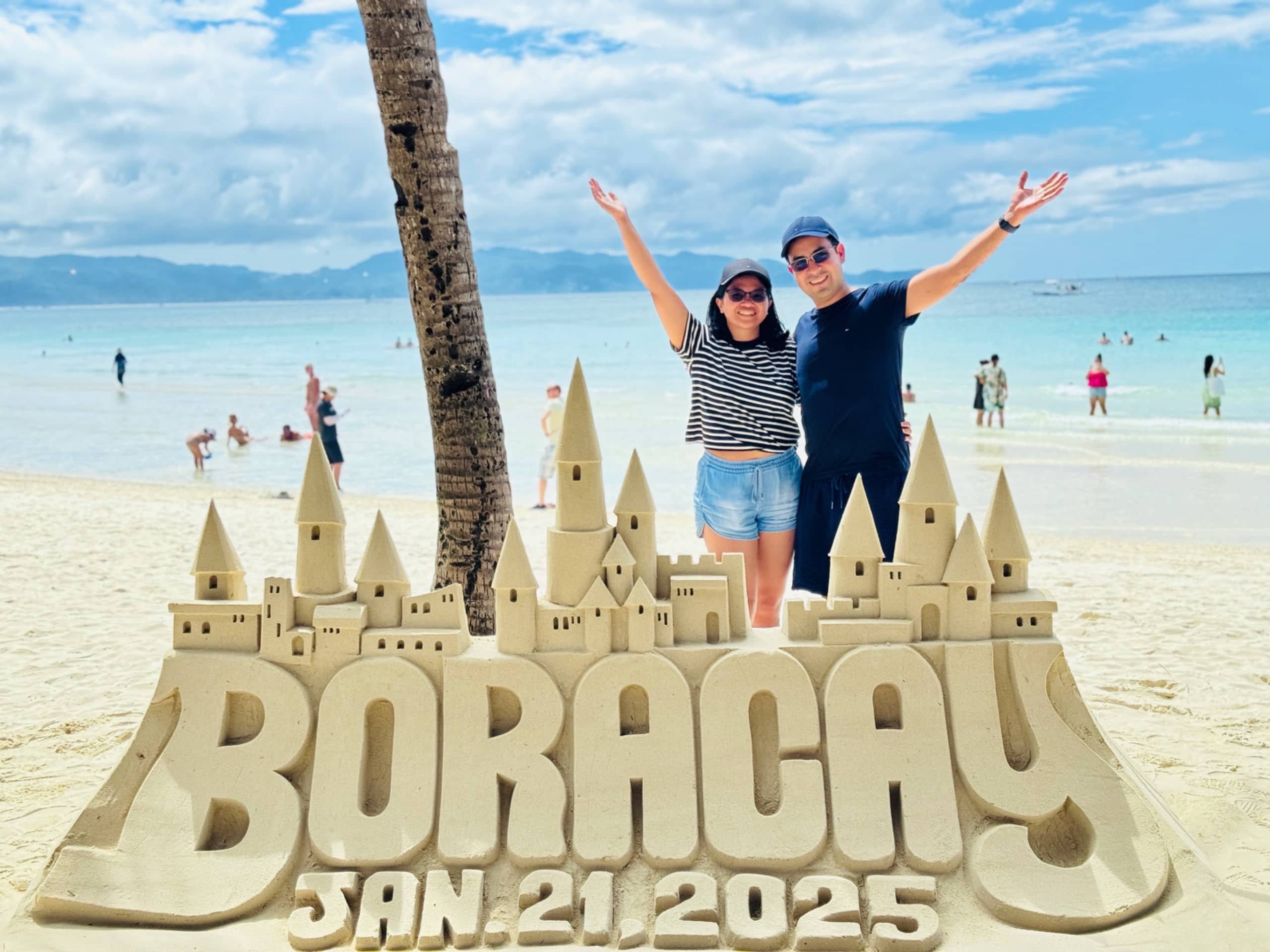 My partner and I behind a sand castle with the words Boracay Jan 21, 2025